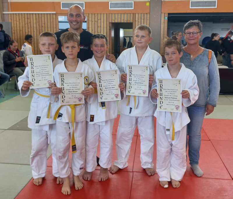 5 junge Judoka präsentieren ihre Urkunde. Ein Betreuer und eine Betreuerin stehen dabei.